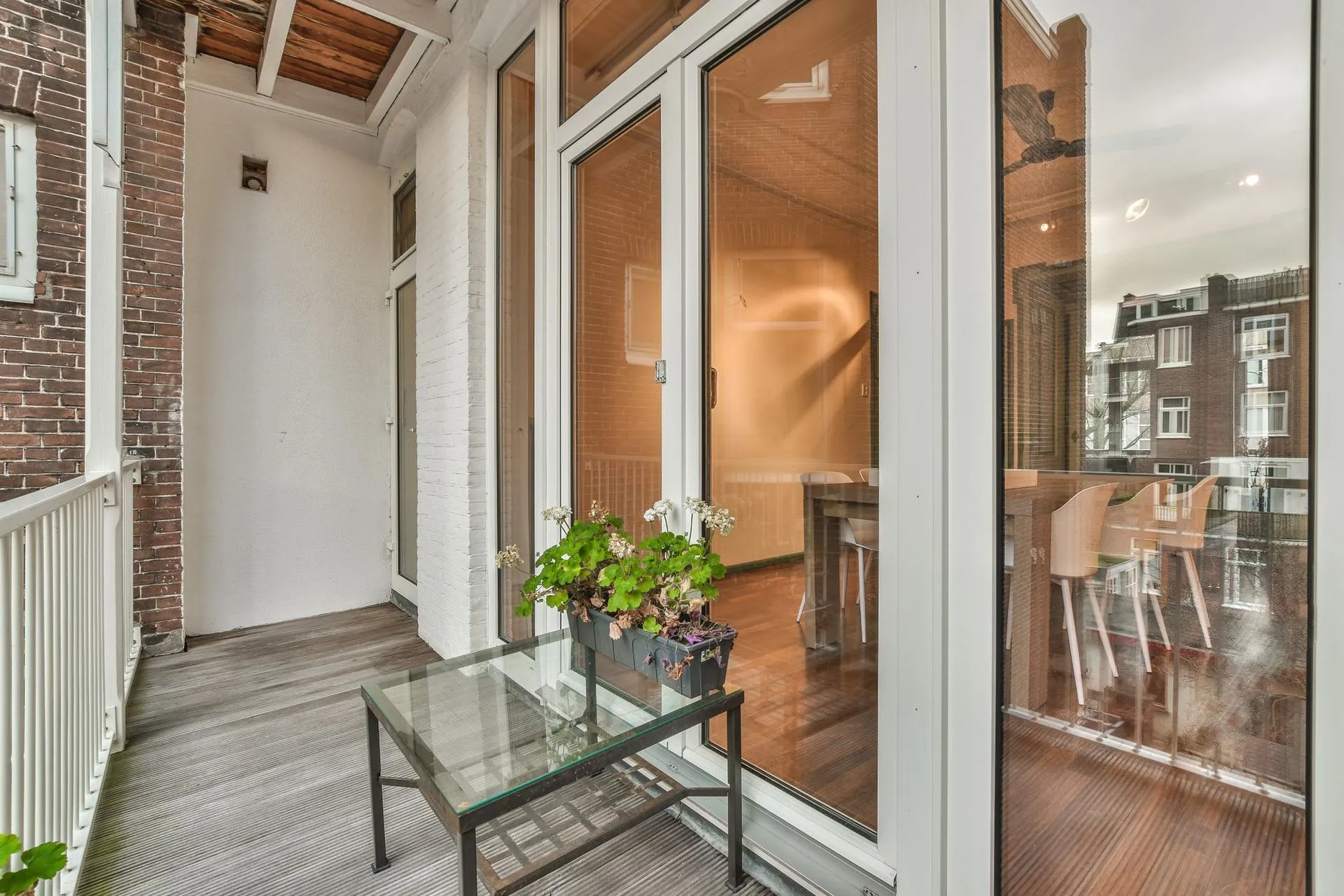 A glass-walled sunroom with a glass-top side table, looking into a bright living space.