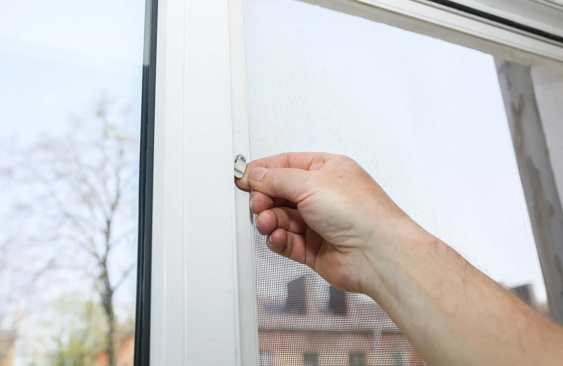 A hand fitting a repaired screen into a window frame.